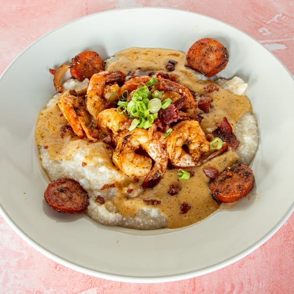 Shrimp and grits with sausage, bacon, and green onions in a white bowl.
