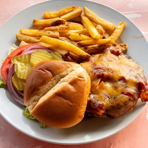 A cheeseburger with pickles, onions, and tomatoes, served with a side of golden french fries.