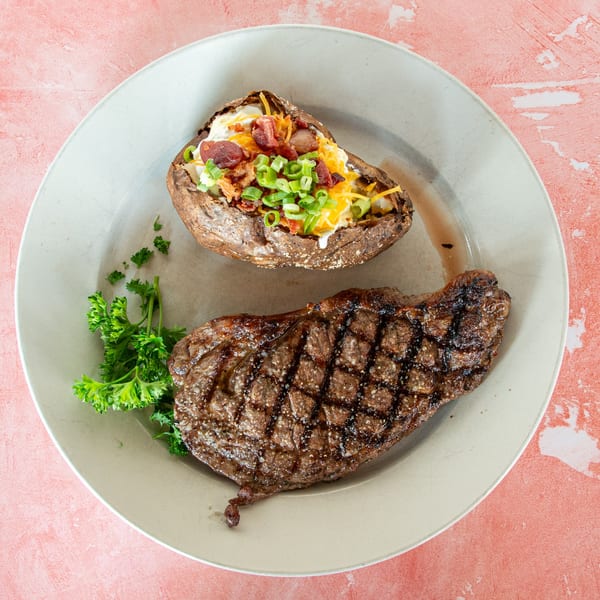 Grilled steak with a loaded baked potato topped with cheese, bacon, and green onions.