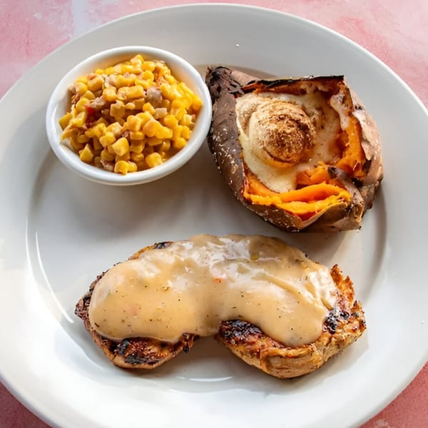 Grilled chicken with gravy, a baked sweet potato with marshmallow, and a side of corn.